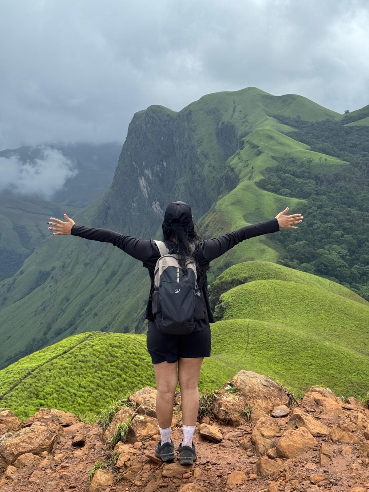 Standing atop a green mountain ridge with arms outstretched